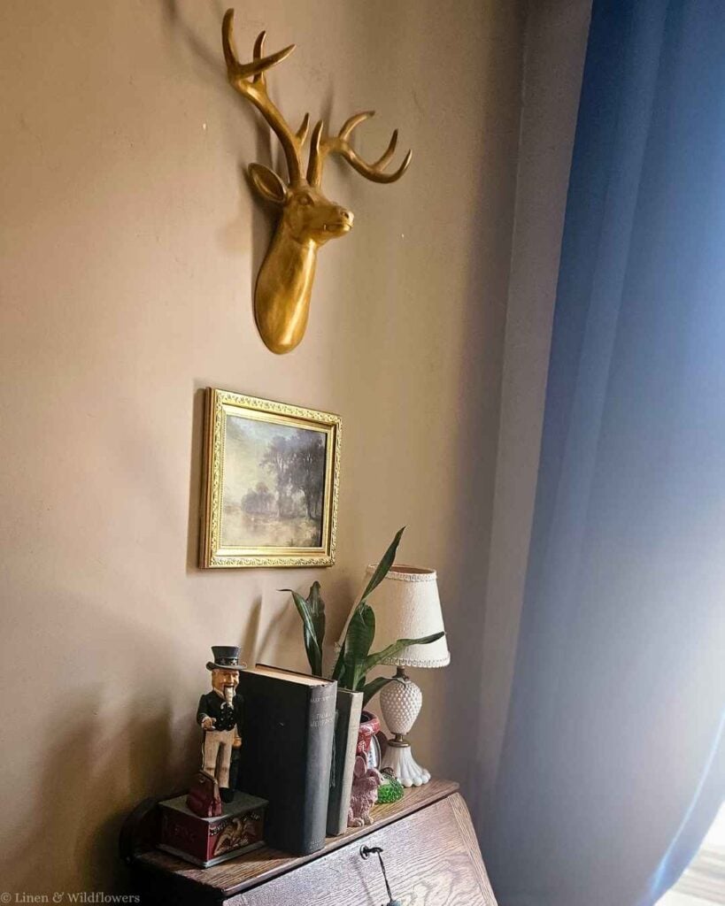 Gold faux deer head mounted above a small vintage landscape painting, the starting point of a vintage gallery wall.