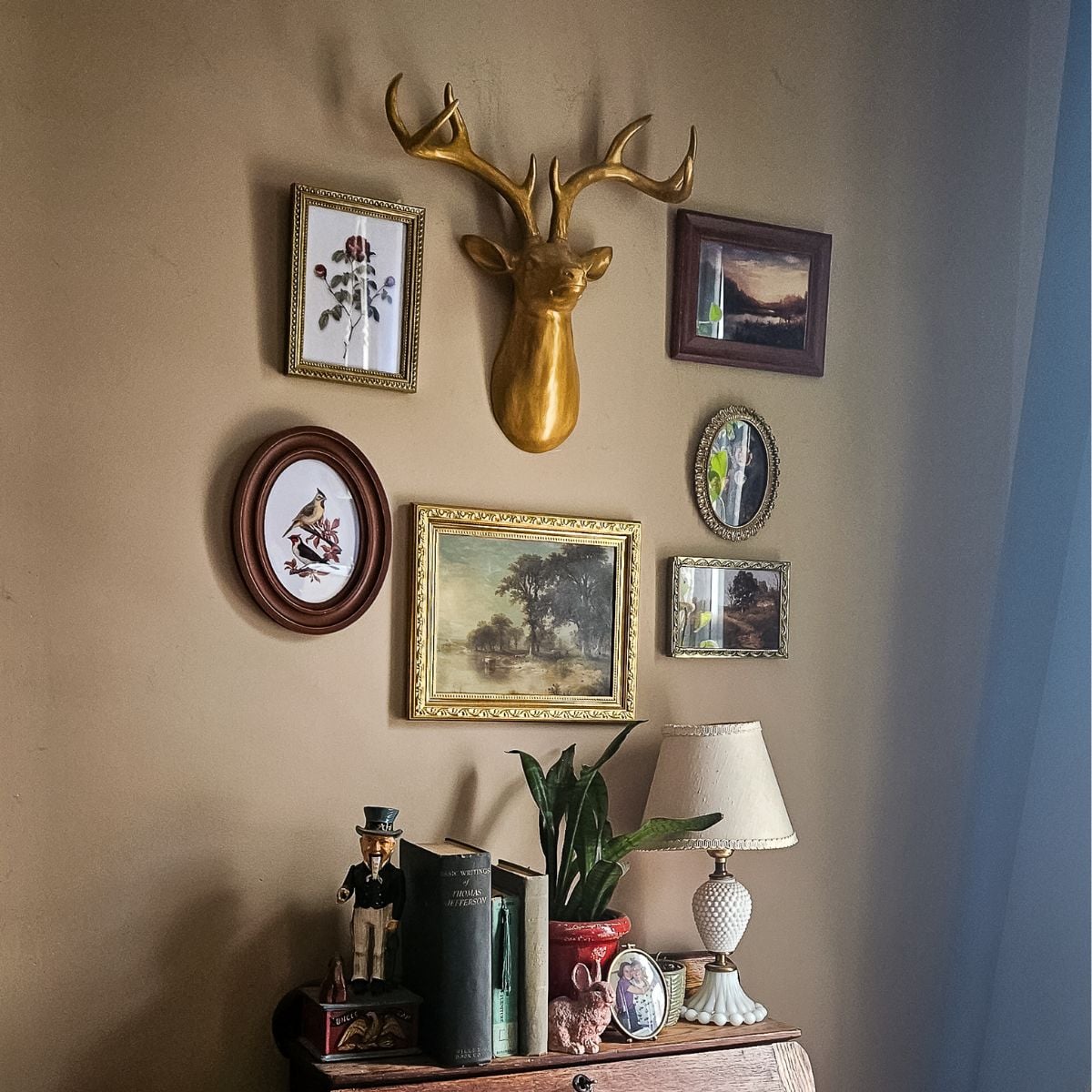 How to create a vintage wall gallery on a budget — finished gallery wall with gold deer head and thrifted frames above an antique desk.