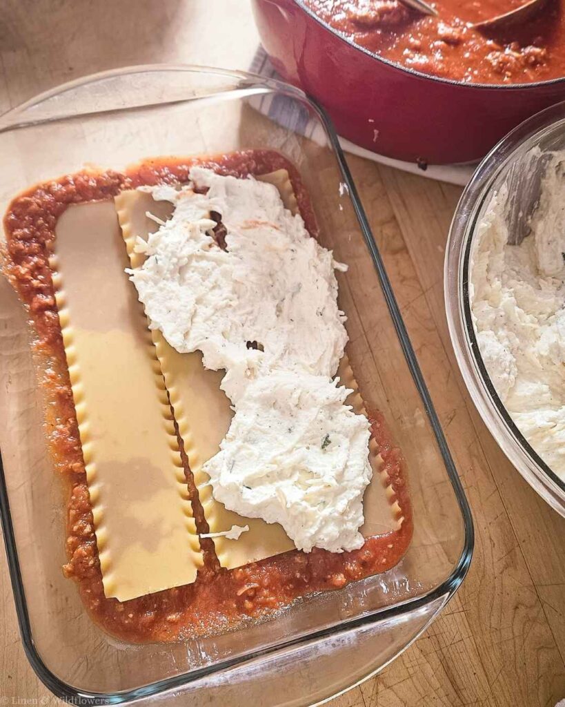 First layer of noodles, sauce, and ricotta filling in a glass baking dish for turkey lasagna.