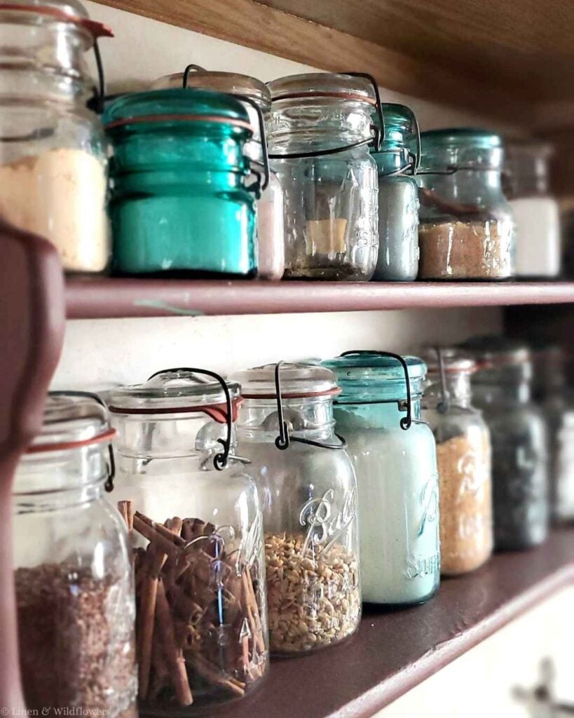 Close-up of teal and clear mason jars filled with pantry staples on a vintage wooden spice shelf.