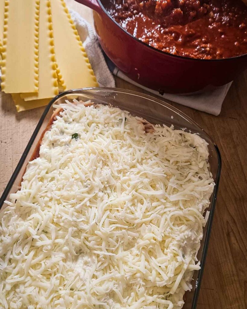 Shredded mozzarella cheese layered on top of assembled turkey lasagna before baking.