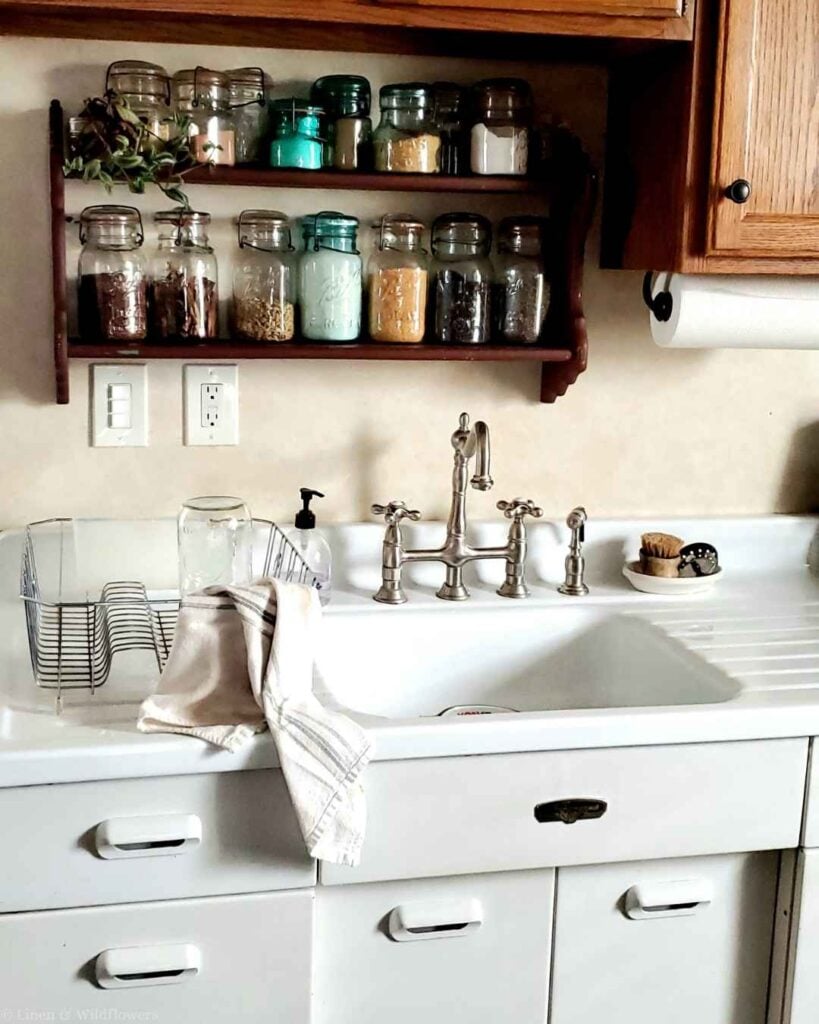 Vintage farmhouse apron sink with bridge faucet and mason jar spice shelf above — budget kitchen charm ideas.