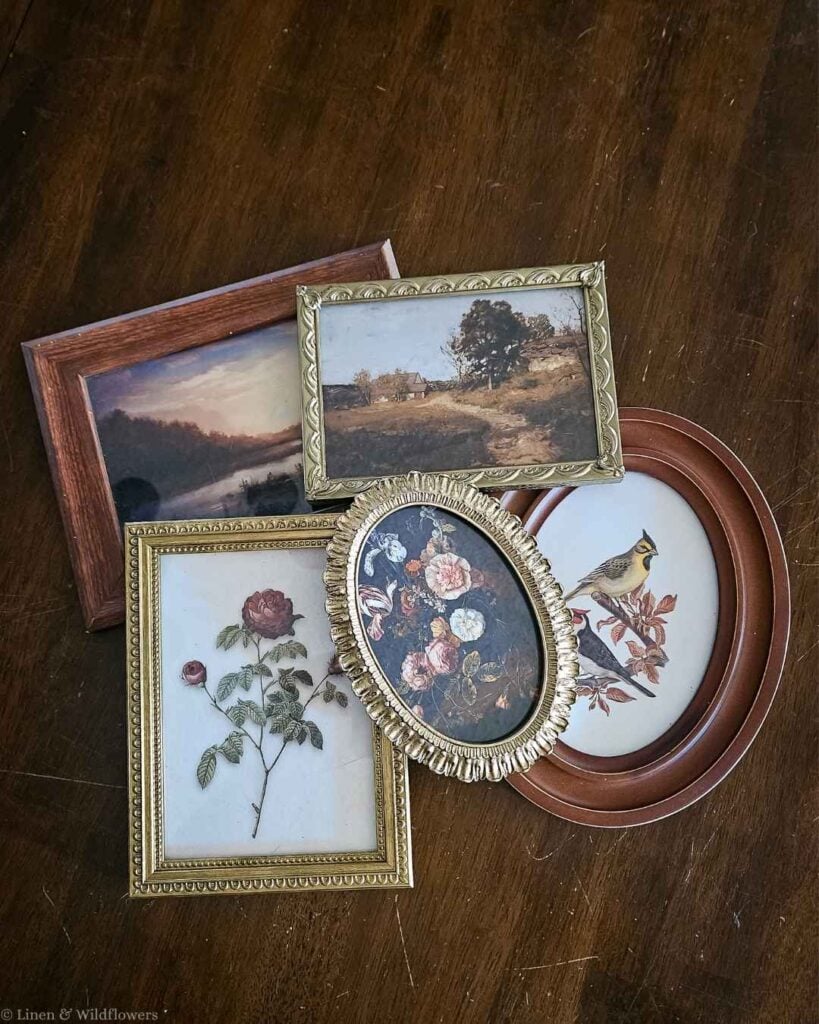Collection of thrifted vintage frames in gold, wood, and oval styles laid out before creating a budget gallery wall.