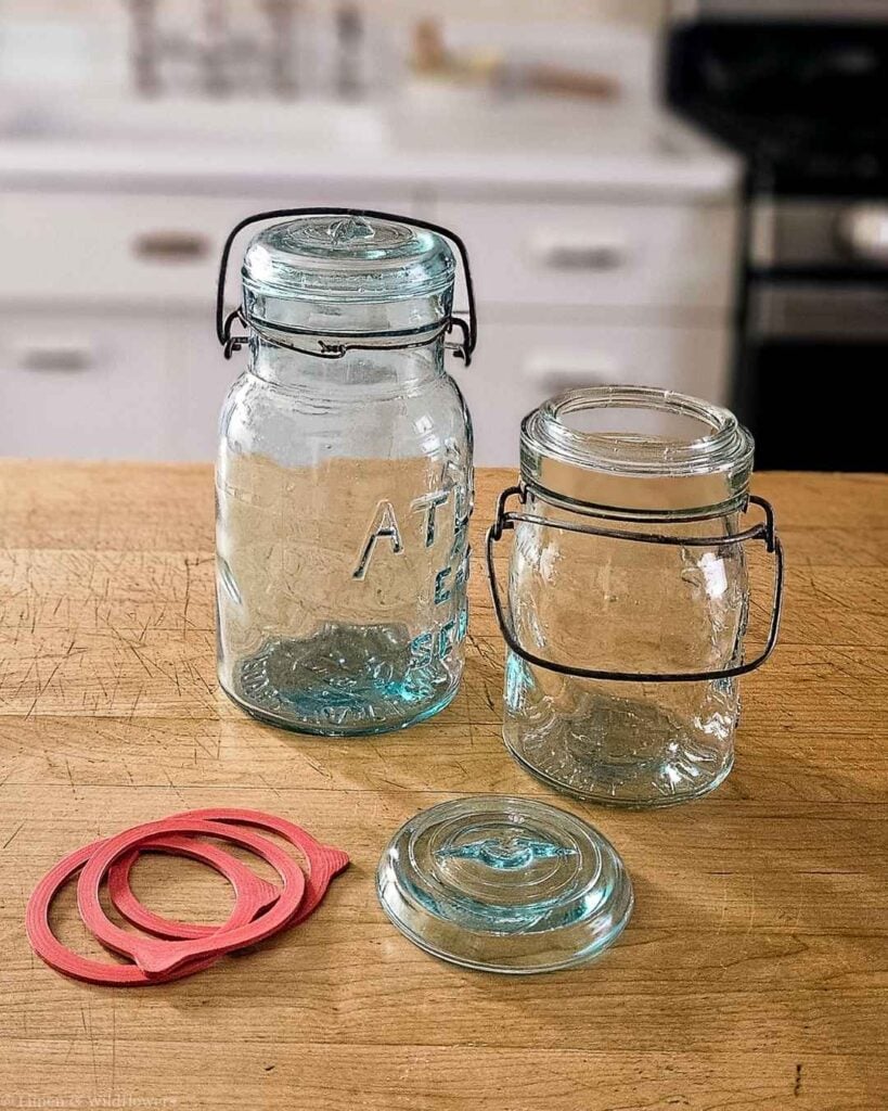 Vintage glass jar parts laid out showing glass lid, wire bail closure, and rubber seal rings.