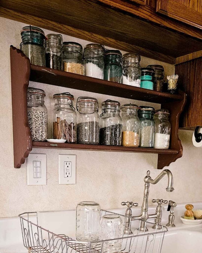 Vintage glass jars with rubber seals filled with pantry staples on a farmhouse kitchen shelf.