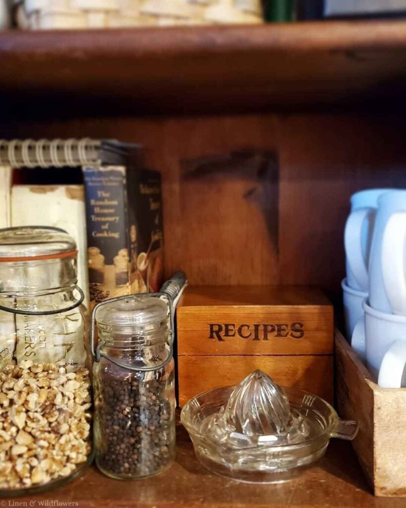 Wooden recipe box, vintage cookbooks, and a glass juicer styled on a kitchen shelf.