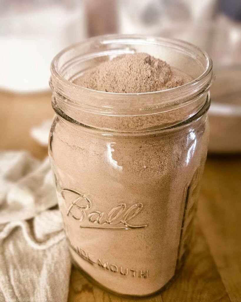 Homemade chocolate cake mix in a Ball wide mouth mason jar on a wooden cutting board.