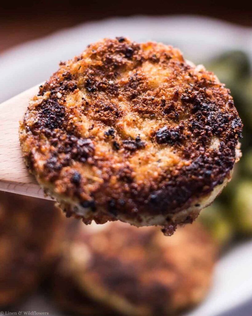 Close-up of a crispy parmesan-crusted fried eggplant round lifted on a wooden spoon.