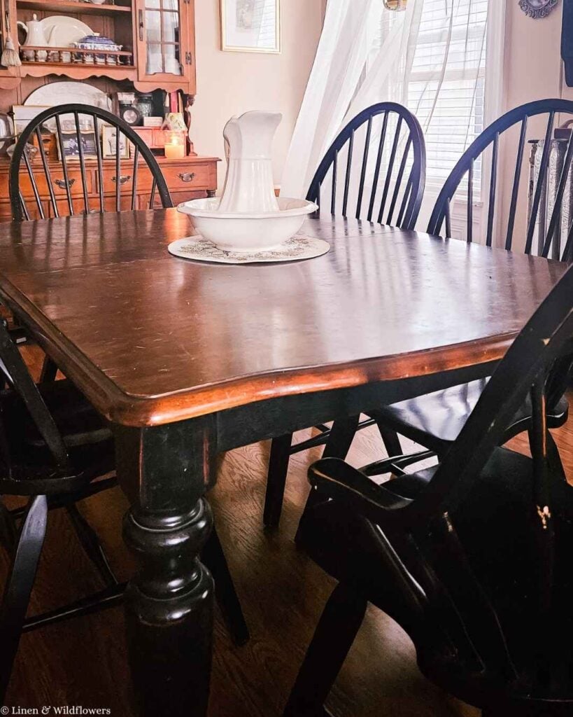 Close up of distressed black painted dining table with natural wood top and Windsor chair detail.