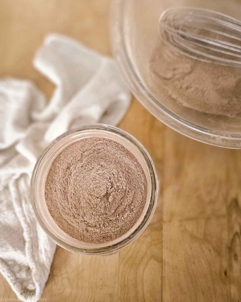 Overhead view of DIY chocolate cake mix in a glass jar next to a linen towel.