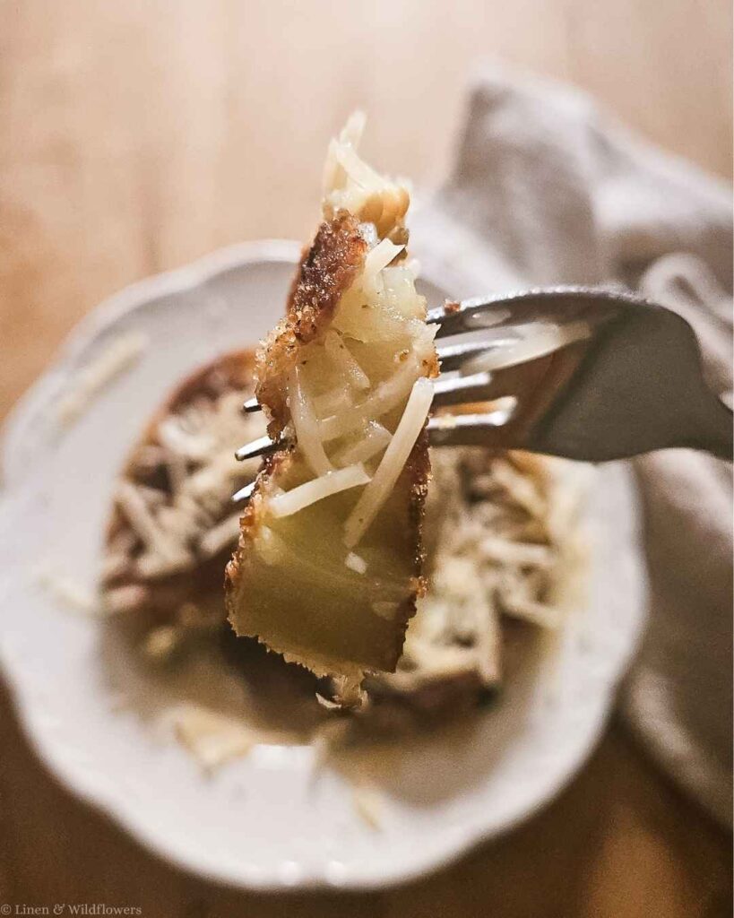 Forkful of fried eggplant topped with melted shaved parmesan cheese.