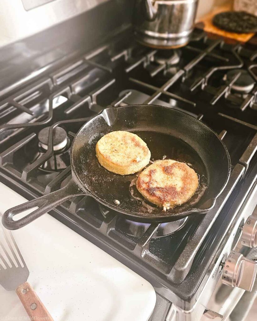 Breaded eggplant rounds frying golden brown in a cast iron skillet on the stove.