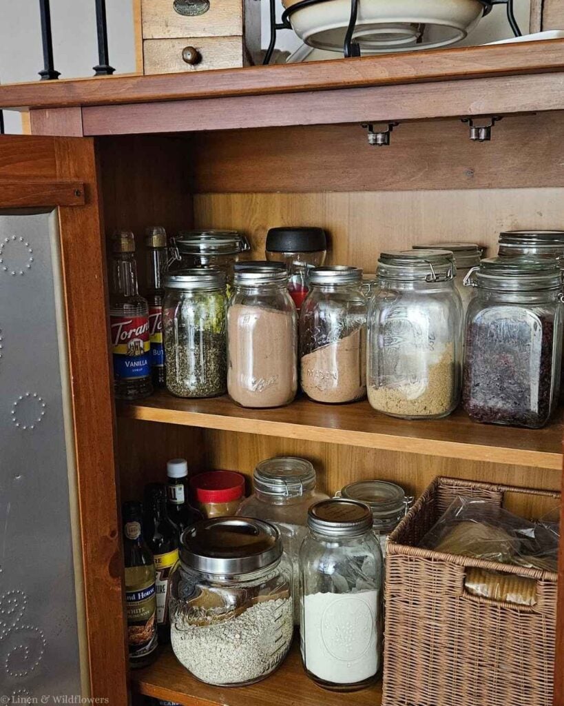 Inside a vintage pie safe repurposed for pantry storage with labeled glass jars.