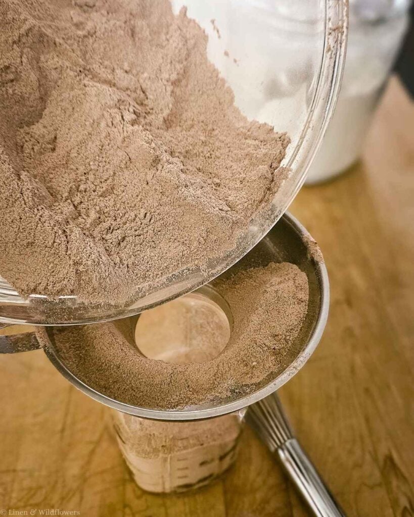 Pouring homemade chocolate cake mix through a funnel into a mason jar for pantry storage.