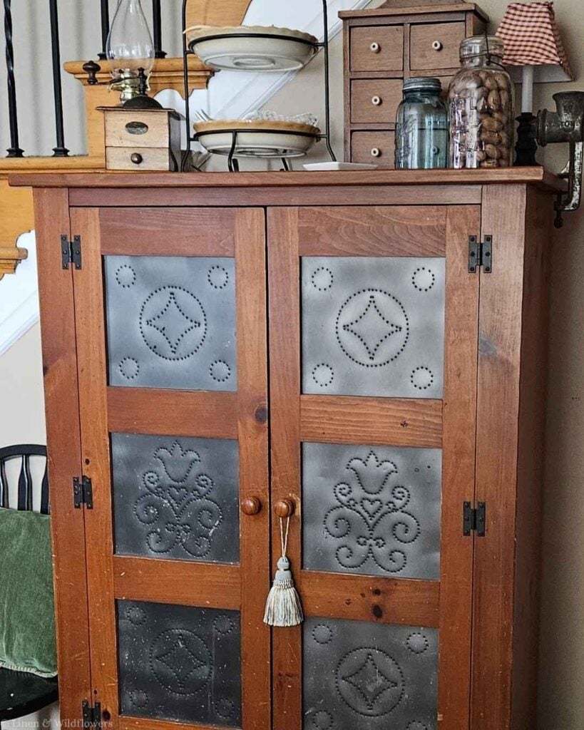 Close-up of punched tin door panels on an antique pie safe with pierced diamond pattern.