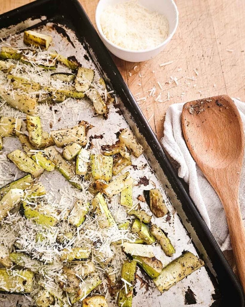 Roasted garlic Parmesan zucchini fresh from the oven on a baking sheet, topped with shredded Parmesan cheese.