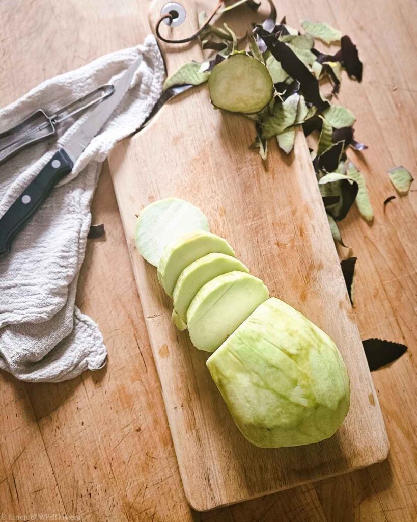 Peeled eggplant sliced into rounds on a wooden cutting board with peelings and knife.