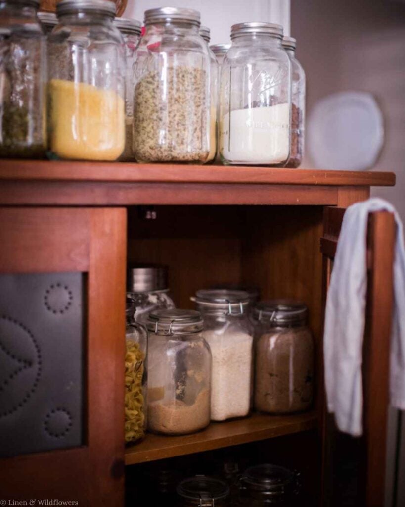 Vintage cabinet shelf organized with glass jars of pasta, sugar, and pantry staples.