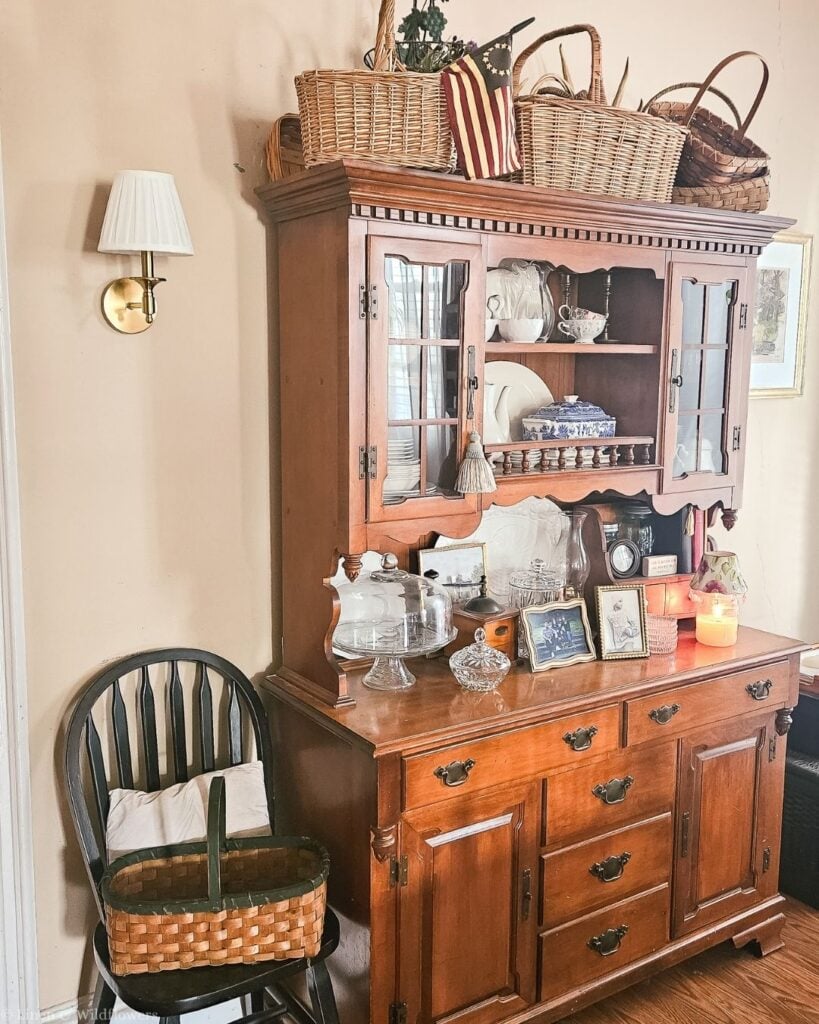 Antique wood hutch topped with vintage baskets and filled with ironstone, blue willow, and a glass cake dome.