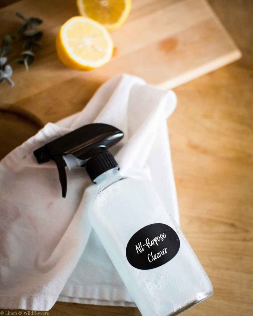 DIY all-purpose cleaner in a labeled glass spray bottle with a lemon half and eucalyptus on a wooden cutting board.