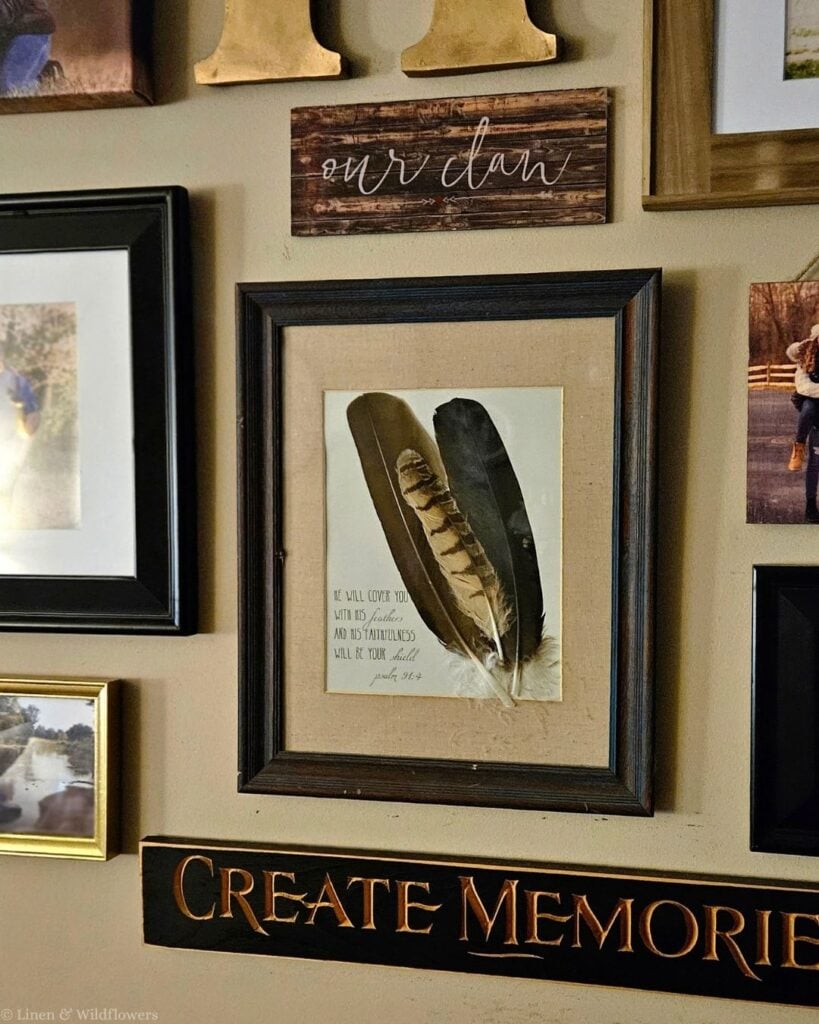 DIY feather art in a dark wood frame with a linen mat and Psalm 91:4 print on a family photo gallery wall.