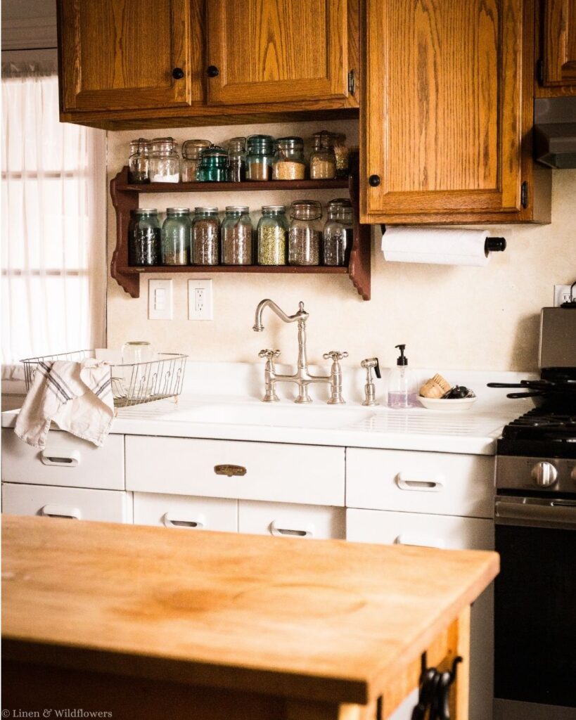 Farmhouse kitchen with a wall shelf of antique blue canning jars filled with pantry staples above a vintage drainboard sink.