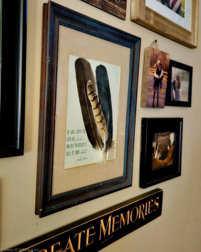 Angled view of framed feather wall art with a linen mat hanging beside family photos above a Create Memories sign.