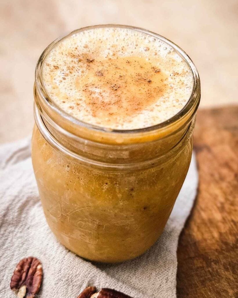 Frothy pumpkin pie smoothie in a glass mason jar on a linen towel with pecans, a cozy fall breakfast idea.