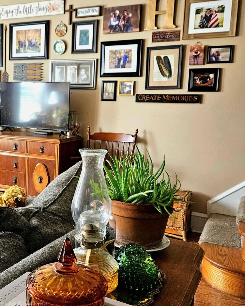 Living room family photo gallery wall with framed feather art, an oil lamp, aloe plant and amber candy dish in the foreground.