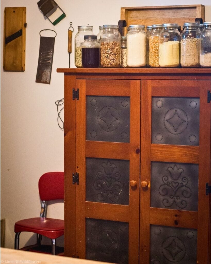 Antique pine pie safe with pierced tin panels topped with mason jars of grains, beans, popcorn and flour for kitchen storage.