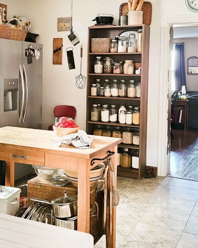 A tall wooden bookcase used as a plastic free kitchen pantry, shelves lined with glass jars of dry goods.