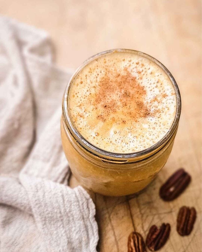 Overhead view of a pumpkin pie smoothie in a mason jar topped with cinnamon and pecans on a cutting board