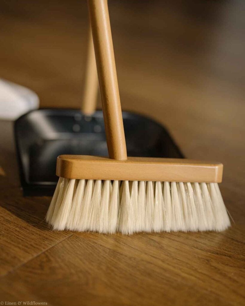 Wooden broom with soft bristles and a black dustpan on a hardwood floor for fast daily sweeping.