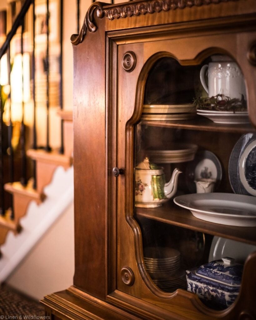 Carved wooden china cabinet displaying a floral teapot, ironstone, and blue and white dishes.