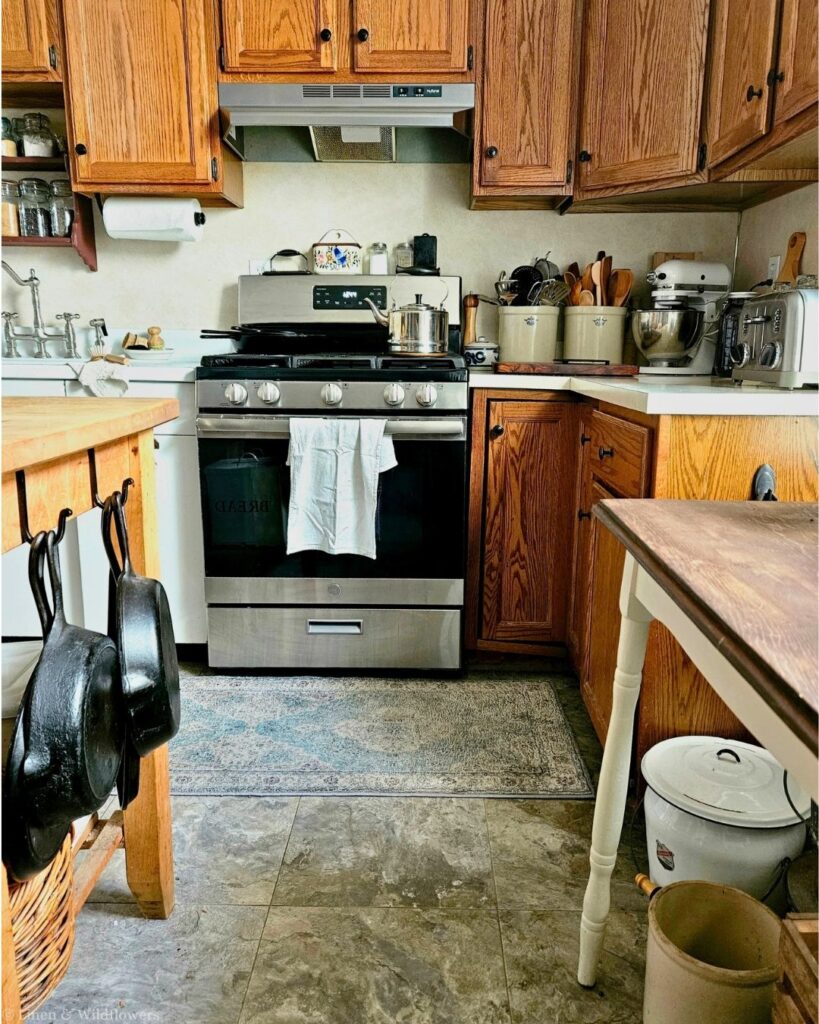 Stainless steel side-by-side refrigerator in a farmhouse kitchen with a crate of canning jars and a vintage table nearby.