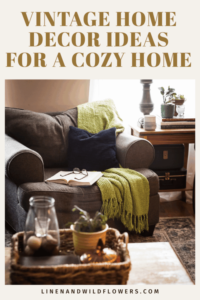 Pinterest pin titled “Vintage Home Decor Ideas for a Cozy Home” showing a gray armchair with a green knit throw, open book and glasses, vintage suitcases under a wood side table, and a woven tray on the coffee table.