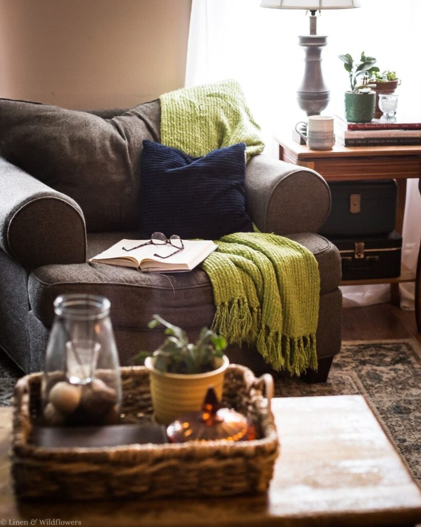 Cozy reading nook with a green throw, open book, and vintage suitcases stacked under a wood side table.