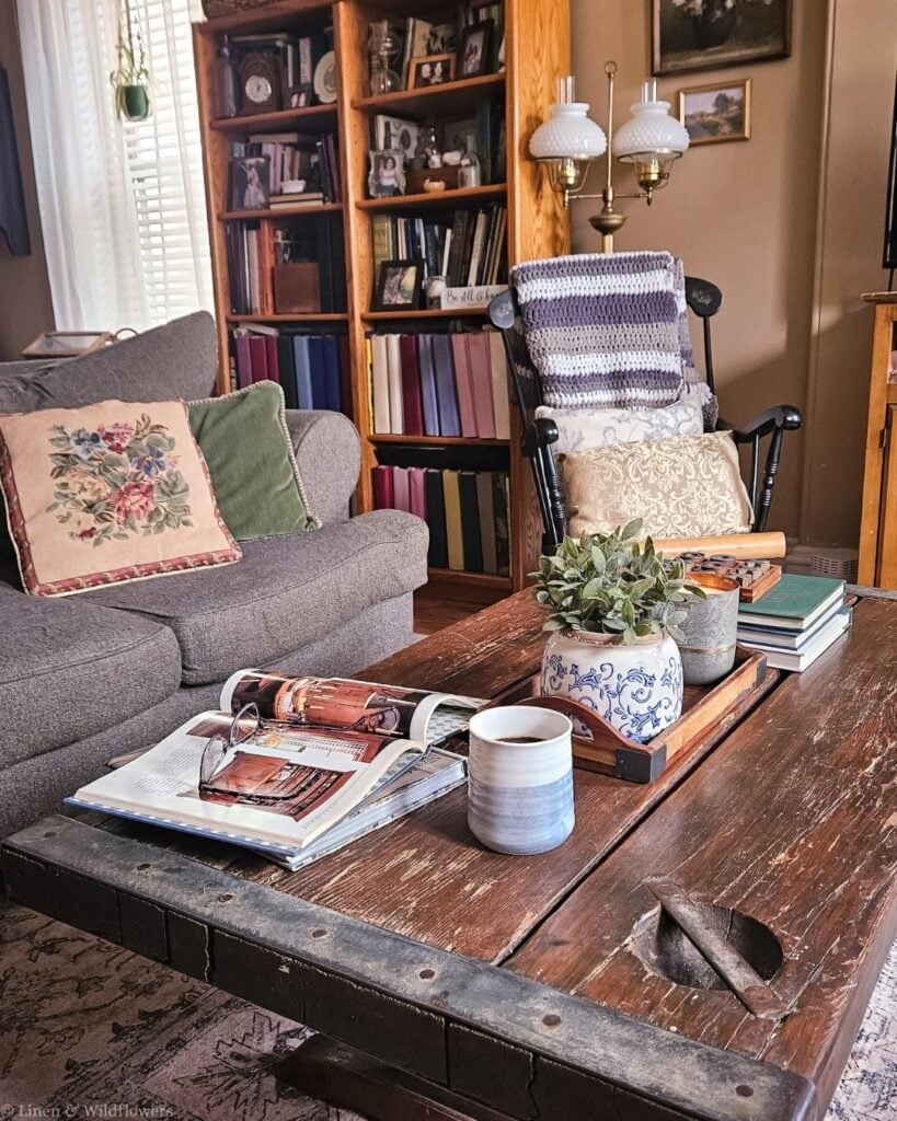 Living room with a distressed vintage wood coffee table, blue and white ginger jar, books, and a bookcase behind.